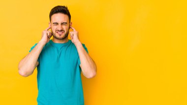 Kafkasyalı genç adam sarı fırında izole edilmiş parmaklarıyla kulaklarını kapatıyor, gürültülü bir ortam yüzünden stresli ve çaresiz..