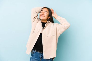 Mavi arka planda izole edilmiş genç bir kadın. Kollarını uzatıyor, rahat bir konumda..