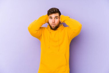 Mor arka planda izole edilmiş genç bir adam kulakları elleriyle kapatıyor ve yüksek sesli sesler duymamaya çalışıyor..