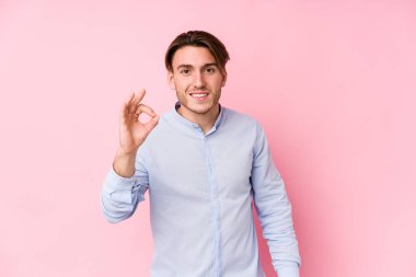 Pembe arka planda poz veren beyaz bir genç adam neşeli ve kendinden emin bir şekilde iyi bir hareket gösteriyor..
