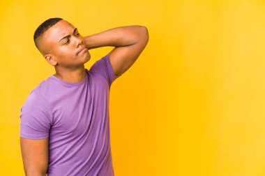 Genç latin adam sarı arka planda izole edilmiş kafasının arkasına dokunuyor, düşünüyor ve bir seçim yapıyor..