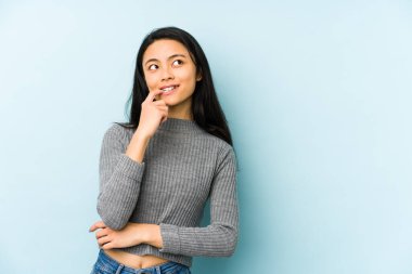 Mavi bir arka planda izole edilmiş genç Çinli kadın rahatlamış bir şeyin fotokopi odasına baktığını düşünüyor..