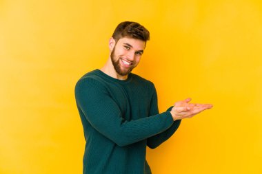 Sarı arka planda izole edilmiş genç beyaz bir adam palmiyesinde bir kopya alanı tutuyor..