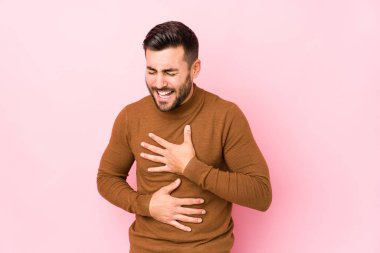 Pembe arka planda yaşayan beyaz bir genç mutlu bir şekilde gülüyor ve ellerini karnının üstünde tutarak eğleniyor..