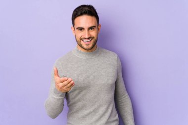 Mor arka planda izole edilmiş genç beyaz adam selamlama jesti olarak kameraya elini uzatıyor..