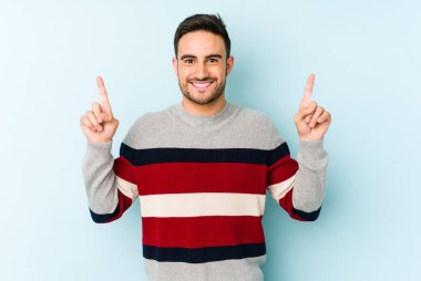Mavi arka planda izole genç beyaz adam işaret iki ön parmakları boş bir boşluk gösteren.