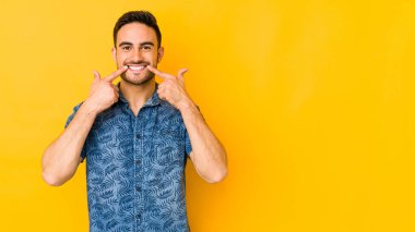 Sarı fırında izole edilmiş genç beyaz adam gülümsüyor, parmaklarını ağıza doğrultuyor..