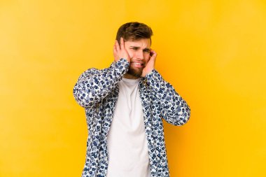 Sarı arka planda izole edilmiş genç beyaz adam elleriyle kulakları örtüyor..