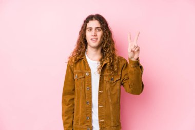 Genç, uzun saçlı, yalnız poz veren, zafer işareti gösteren ve gülümseyen adam..