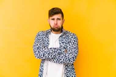 Sarı arka planda izole edilmiş genç beyaz adam yanakları patlatır, yorgun bir ifadeye sahiptir. Yüz ifadesi kavramı.