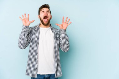 Kafkasyalı genç adam mavi arka planda izole edilmiş gökyüzüne haykırıyor, yukarı bakıyor, hayal kırıklığına uğramış..