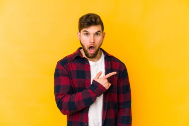 Sarı arka planda izole edilmiş genç beyaz adam yan tarafı işaret ediyor.