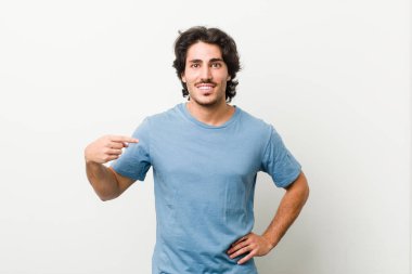 Genç yakışıklı bir adam beyaz arkaplanlı birine karşı gömlek fotokopisini elle gösteren, gururlu ve kendinden emin.