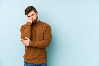 Mavi arka planda izole edilmiş, üzgün ve dalgın hisseden, kopyalama alanına bakan genç beyaz bir adam..