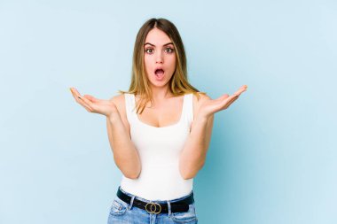 Mavi arka planda izole edilmiş genç beyaz kadın şaşırdı ve şok oldu..