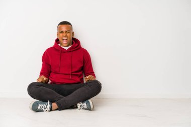 Yerde tek başına oturan genç latin adam çok sinirli ve agresif çığlıklar atıyor..