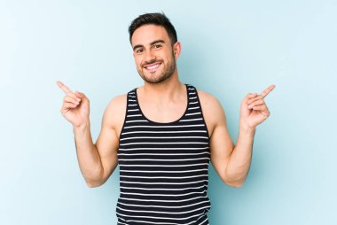 Mavi arka planda izole edilmiş genç beyaz adam farklı kopya alanlarını gösteriyor, birini seçiyor, parmaklarıyla gösteriyor.