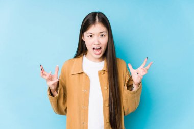 Mavi arka planda poz veren Çinli genç bir kadın öfkeyle bağırıyor..