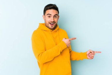 Kafkasyalı genç adam mavi arka planda izole edilmiş. İşaret parmağıyla işaret ettiği için heyecanlı..