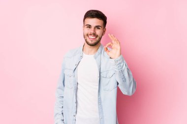 Beyaz arka planda poz veren beyaz tenli genç bir iş adamı neşeli ve kendinden emin bir şekilde hareket ediyor..