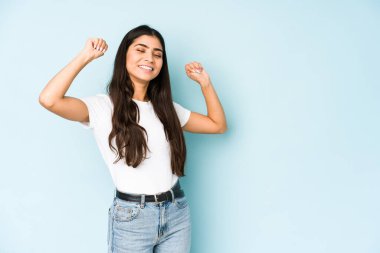 Mavi arka plandaki genç Hintli kadın özel bir günü kutluyor, kollarını enerji ile kaldırıyor..