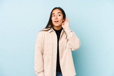 Genç bir kadın mavi arka planda izole edilmiş bir şekilde bir dedikoduyu dinlemeye çalışıyor..