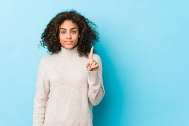 Genç Afro-Amerikan kıvırcık saçlı kadın parmaklarıyla bir numarayı gösteriyor..