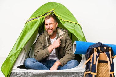 Beyaz arka planda izole edilmiş bir çadırda kıdemli biri gülümsüyor ve boş alanda bir şey gösteriyor..