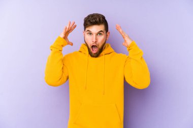 Mor arka planda kalan genç adam zaferi ya da başarıyı kutluyor, şaşırıyor ve şok oluyor..