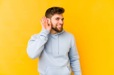 Sarı arka planda izole edilmiş genç beyaz bir adam bir dedikoduyu dinlemeye çalışıyor..