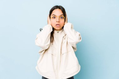 Genç, melez, İspanyol bir kadın. Kulaklarını ellerinle kapatıyor. Gürültülü sesler duymamaya çalışıyor..