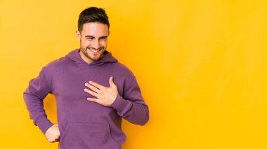 Kafkasyalı genç adam sarı fırında izole edilmiş gülüyor, ellerini yüreğine koyuyor, mutluluk kavramını koruyor..