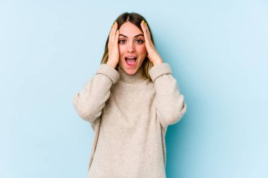 Mavi arka planda izole edilmiş genç beyaz kadın yüzünün yarısını palmiyeyle kaplarken eğleniyor..