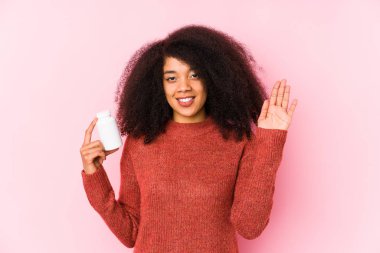Vitaminlerini tutan genç afro bir kadın. Elinde beş numaralı vitaminli, neşeli parmakları olan Afro bir kadın var..