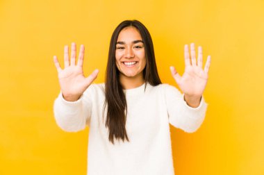 Sarı arka planda izole edilmiş genç bir kadın on numarayı elleriyle gösteriyor..