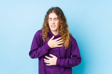 Uzun saçlı adam mutlu mesut gülüyor ve ellerini karnının üstünde tutarak eğleniyor..