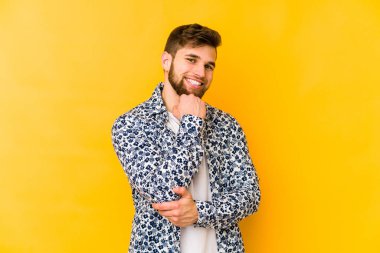 Sarı arka planda izole edilmiş genç, mutlu ve kendinden emin gülümseyen, elleriyle çenesine dokunan beyaz bir adam..