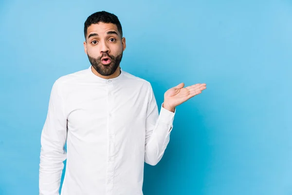 Hombre Latino Joven Sobre Fondo Azul Aislado Impresionado Sosteniendo Espacio — Foto de Stock