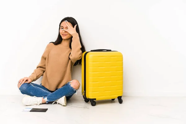 若いです中国人旅行者女性座っています床にスーツケースで隔離された点滅でカメラで指を通して 恥ずかしがり屋カバー顔 — ストック写真
