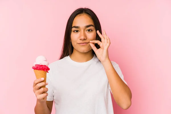 Young asian woman holding a ice cream isolated with fingers on lips keeping a secret.