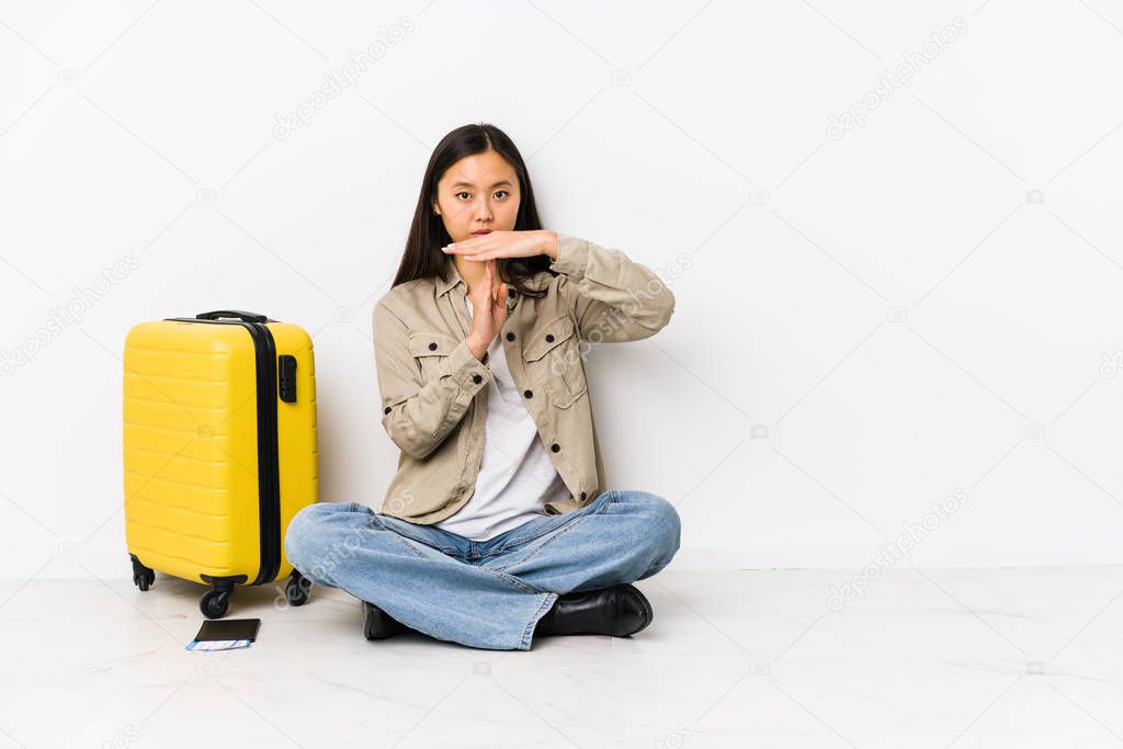 Young chinese traveler woman sitting holding a boarding passes showing a timeout gesture.