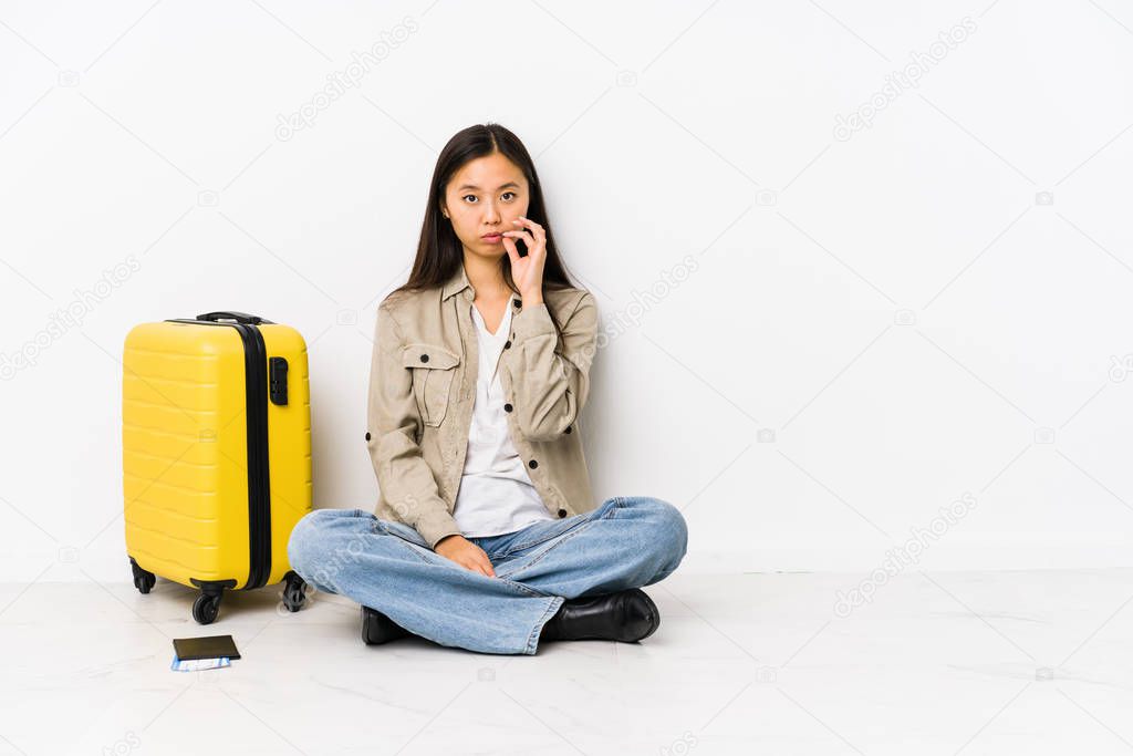 Young chinese traveler woman sitting holding a boarding passes with fingers on lips keeping a secret.