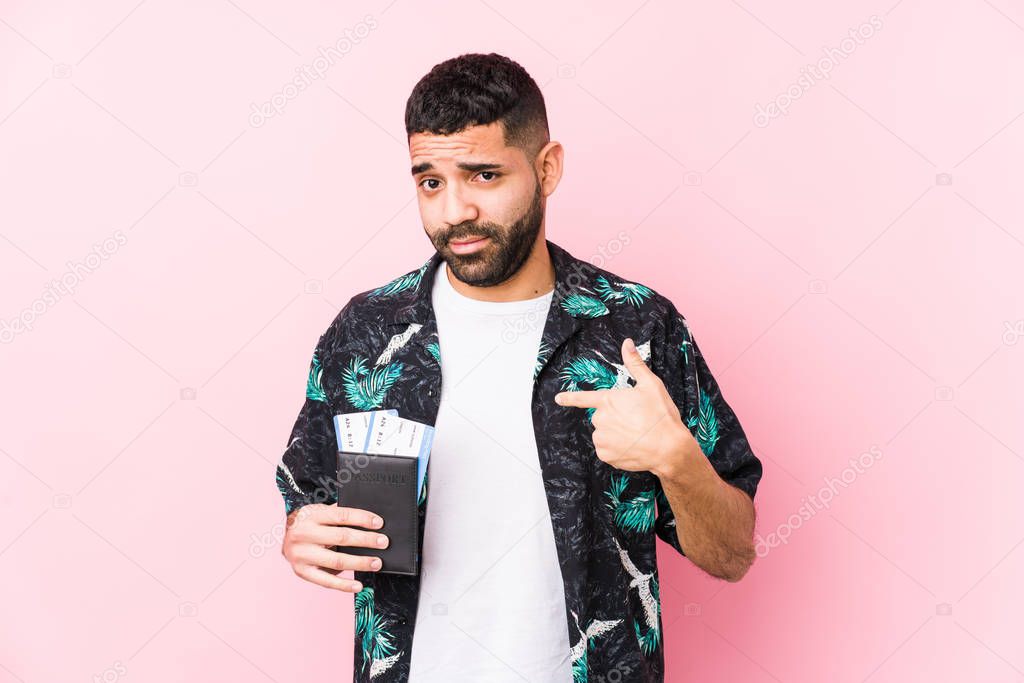 Young arabian cool man holding a boarding passes isolated pointing with finger at you as if inviting come closer.