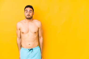 Sarı arka planda yalıtılmış beyaz mayo giyen genç, omuzları omuzları omuzları açık, gözleri açık beyaz bir adam..