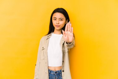 Sarı arka planda izole edilmiş genç Çinli bir kadın elini uzatmış, dur işareti göstererek seni engelliyor..