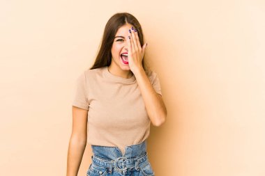 Beyaz tenli genç bir kadın bej arka planda izole edilmiş. Yüzünün yarısını palmiye ile kaplayarak eğleniyor..