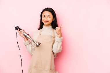 Elinde mikser tutan genç Çinli bir kadın izole edilmiş gülümsüyor ve boş alanda bir şey gösteriyor..