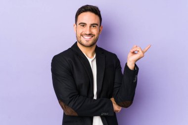 Mor arka planda izole edilmiş genç beyaz adam işaret parmağıyla işaret ederek gülümsüyor..