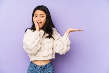 Mor arka planda izole edilmiş genç Çinli bir kadın avuç içinde fotokopi alanı tutuyor, el üstünde tutuyor. Şaşırmış ve mutlu..