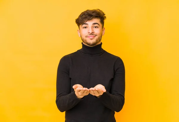 Joven Árabe Aislado Sobre Fondo Amarillo Sosteniendo Algo Con Palmas — Foto de Stock